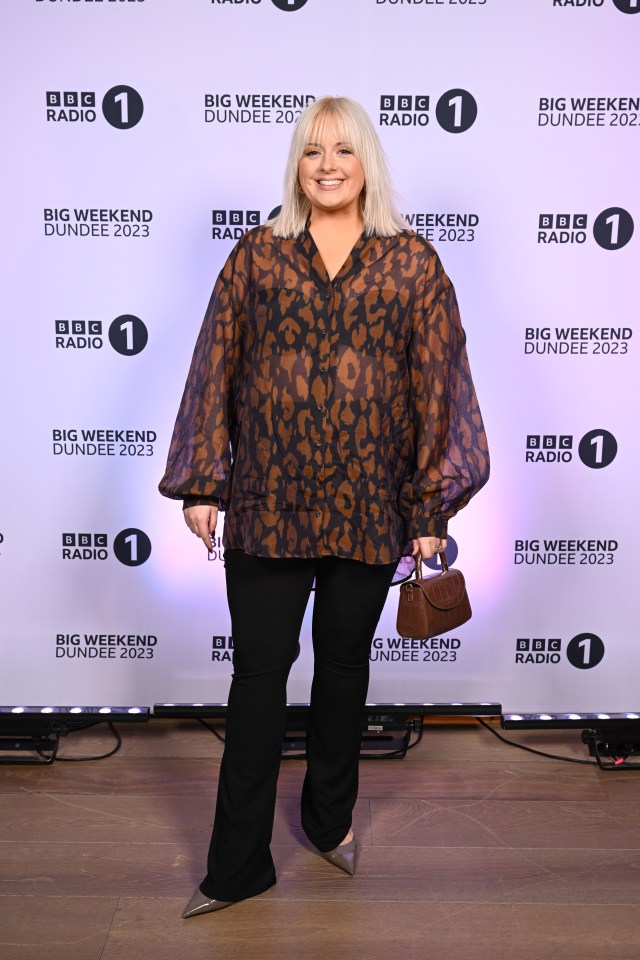 a woman stands in front of a wall that says big weekend dundee 2023