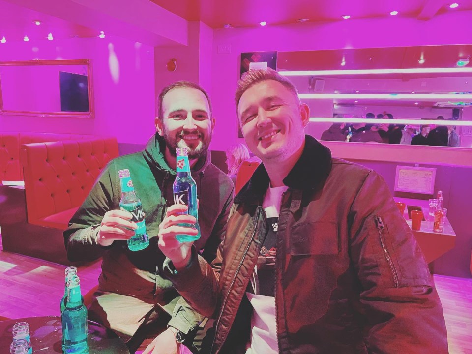 two men holding up bottles of blue liquid with the letter k on them