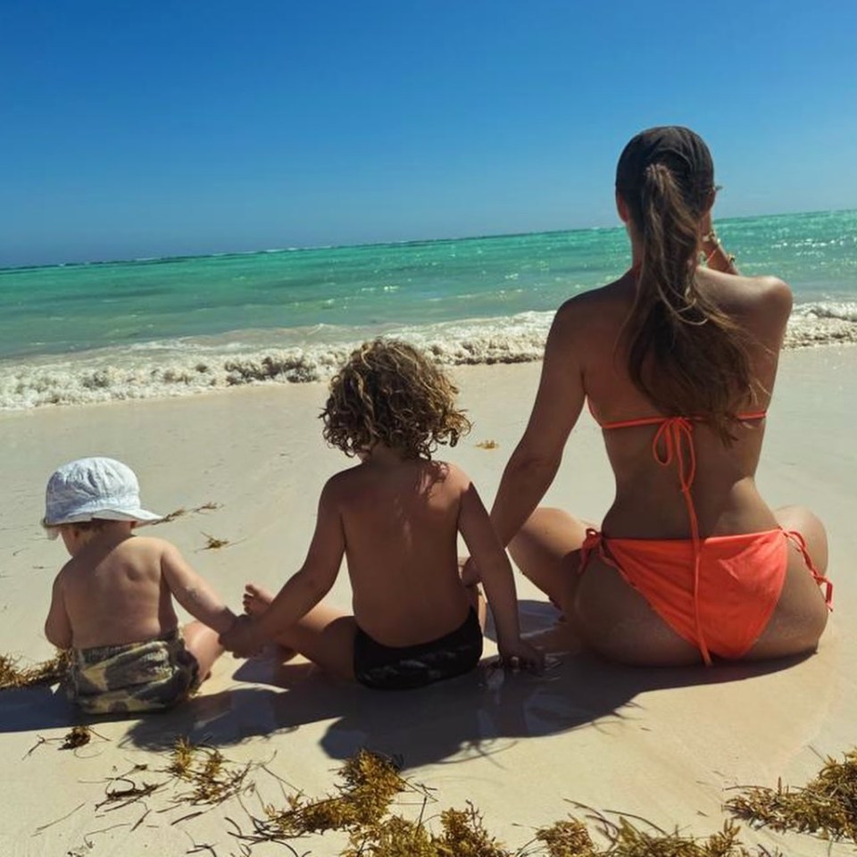 a woman in an orange bikini sits on the beach with two children