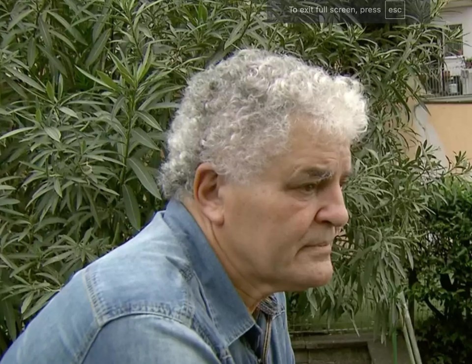 a man with curly white hair is standing in front of a bush and a screen that says to exit full screen press esc