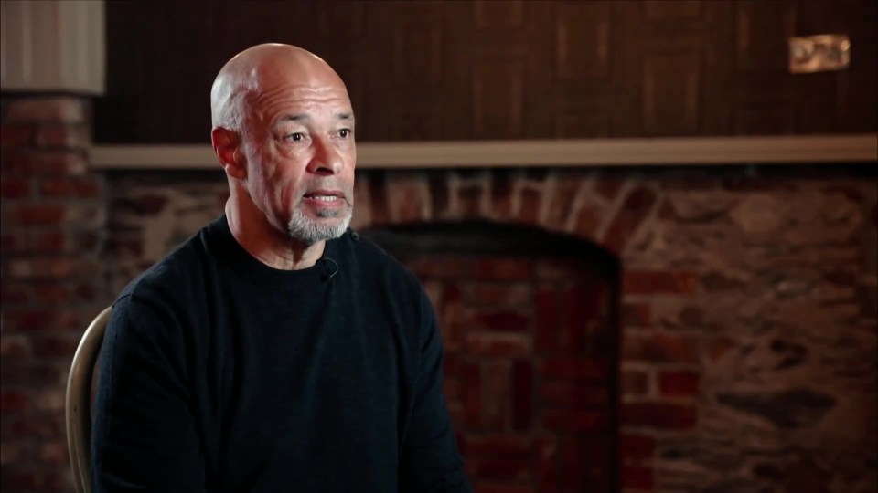 a man in a black sweater sits in front of a fireplace