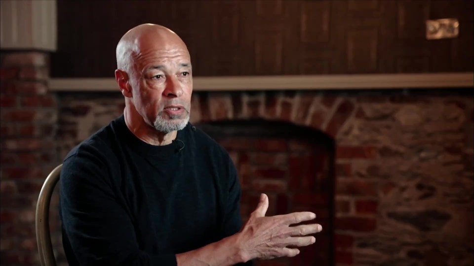 a man in a black shirt is sitting in front of a fireplace