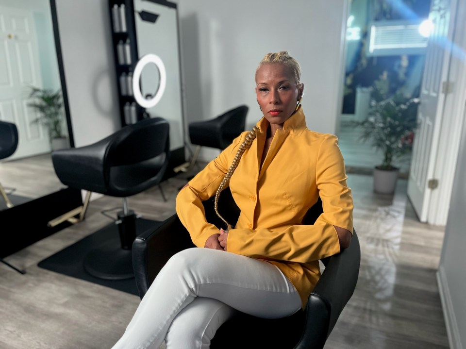 a woman in a yellow jacket sits in a chair in a salon