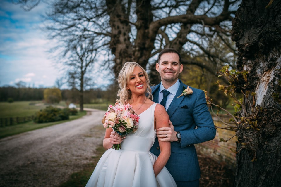 a bride and groom pose for a picture in front of a tree