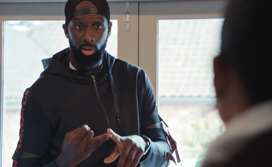 a man with a beard wearing a black jacket and a hat that says ' reebok ' on it