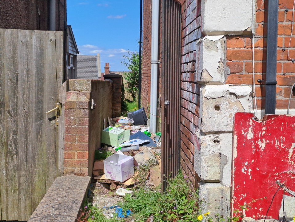 Heaps of rubbish are discarded in an alleyway beside the abandoned home