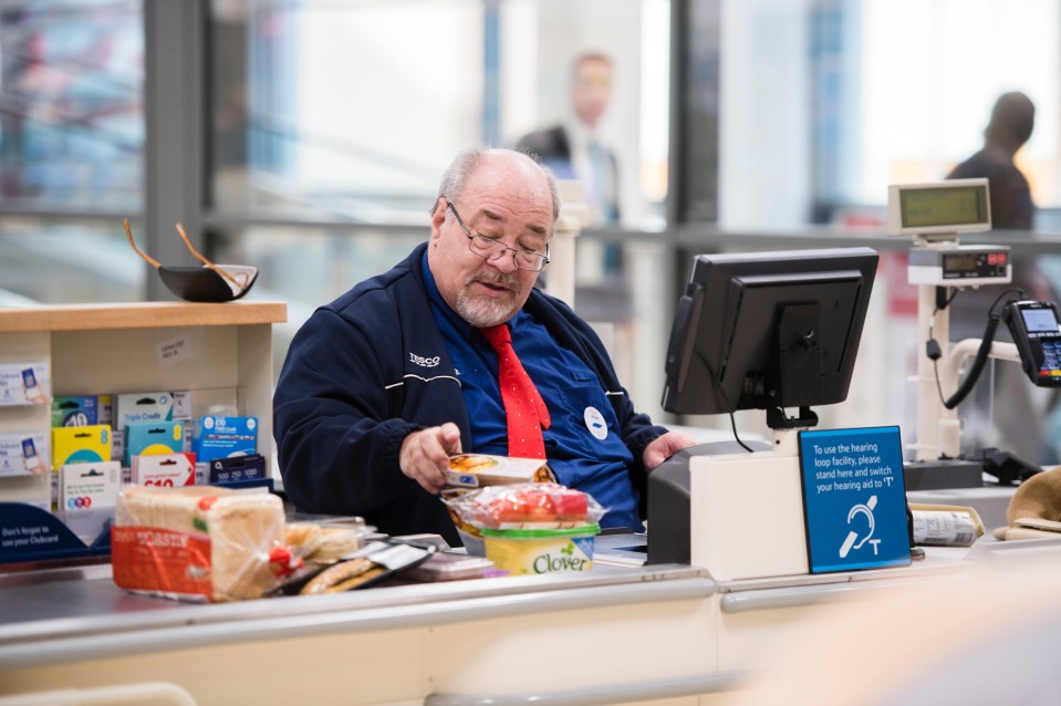 a man in a tesco uniform stands at a cash register