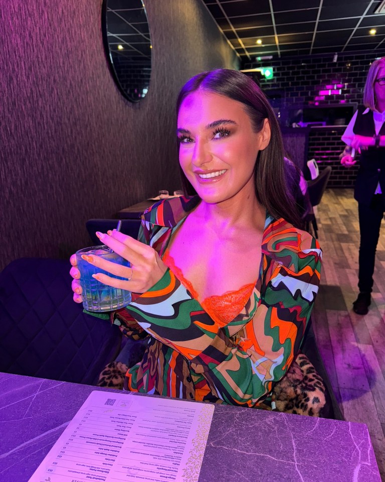 a woman holding a blue drink in front of a menu