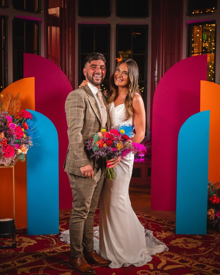 a bride and groom pose in front of a colorful backdrop