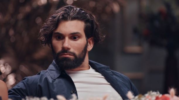 a man with a beard is sitting at a table with flowers .