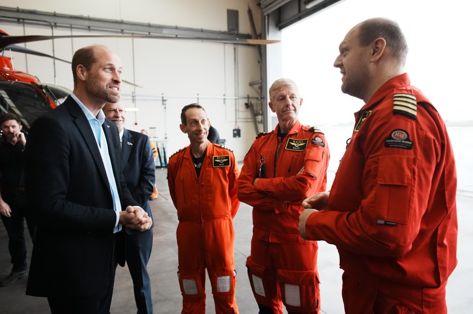 a man in a suit talks to a group of men in red jumpsuits