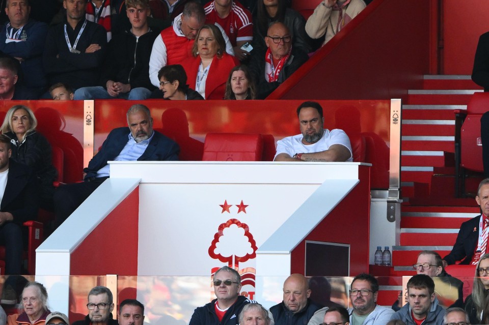 a man in a white shirt sits in the stands watching a game