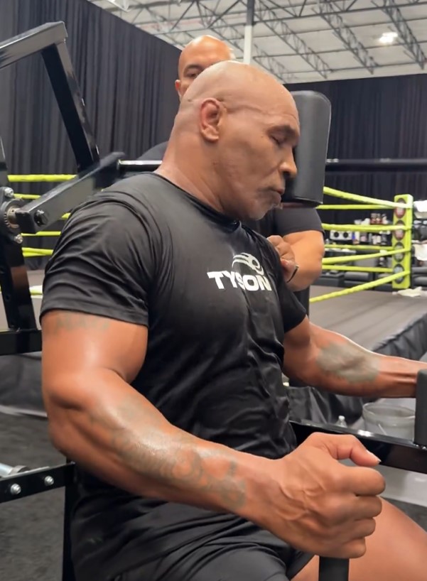 a man wearing a black shirt that says tyson sits on a machine