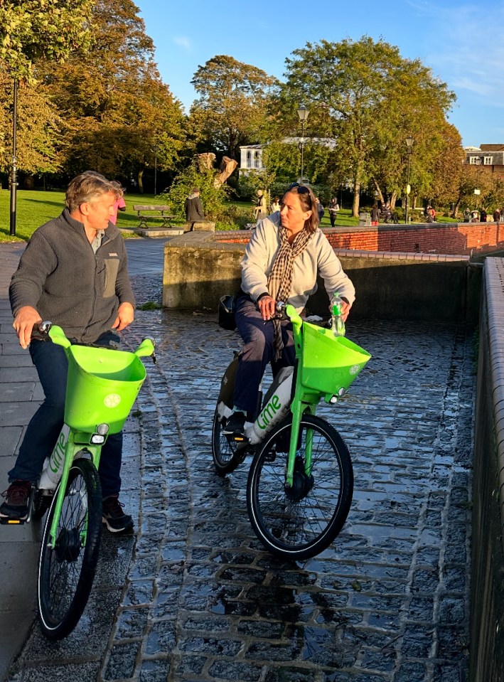 a man and a woman ride lime bikes on a cobblestone street