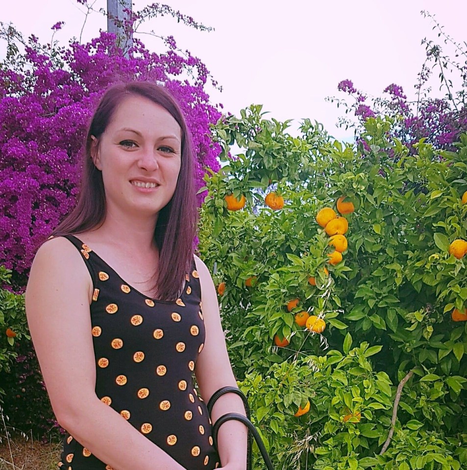 a woman in a black polka dot dress stands in front of a bush with oranges