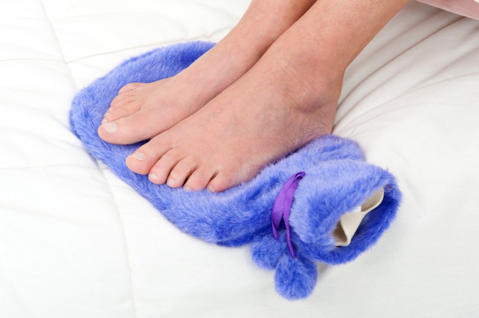 a person laying on a bed with their feet on a purple hot water bottle