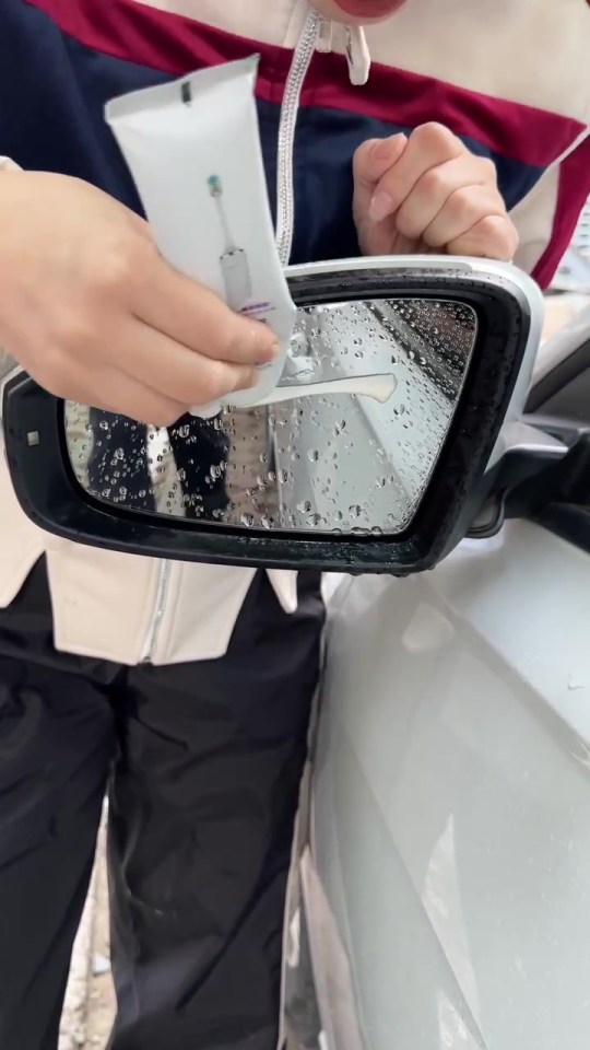 a person is cleaning a car rear view mirror with a tube of toothpaste