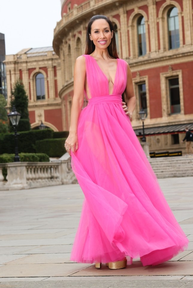 a woman in a bright pink dress stands in front of a building