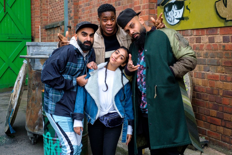 a group of people posing in front of a brick wall with graffiti on it