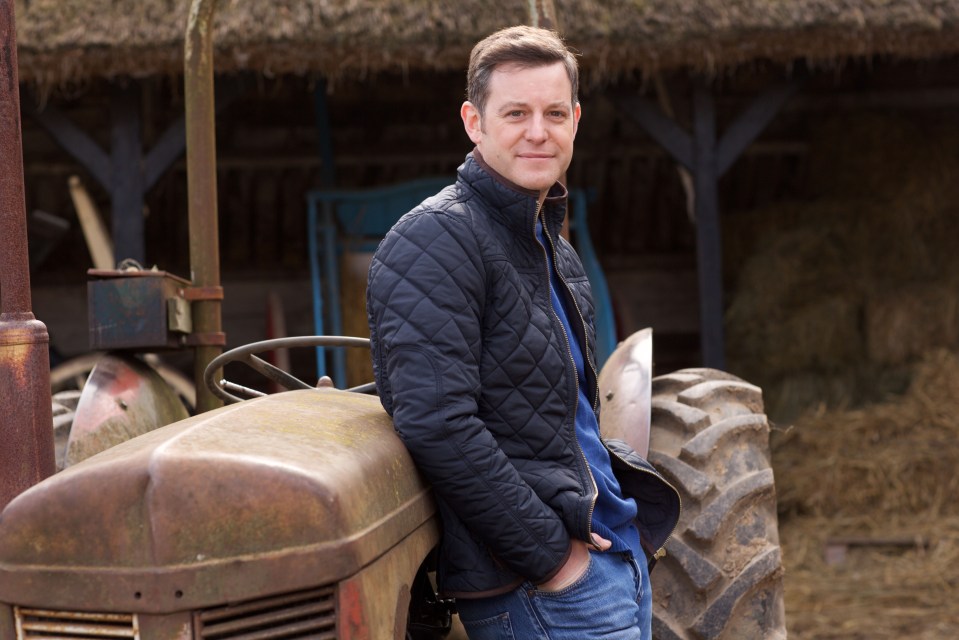 a man in a black jacket leans against an old rusty tractor