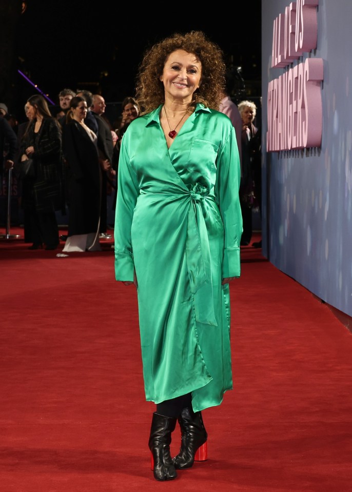 a woman in a green dress stands on a red carpet in front of a sign that says all of us strangers