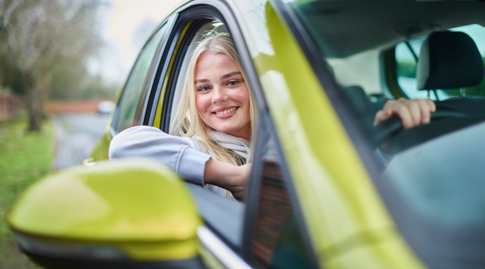 a woman is smiling while sitting in a yellow car