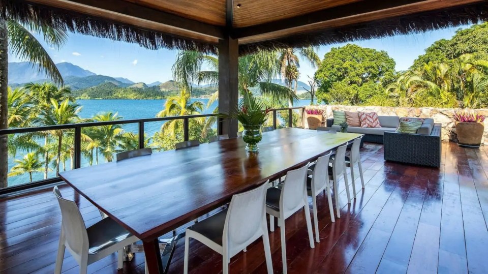 a large wooden table and chairs on a balcony overlooking a body of water