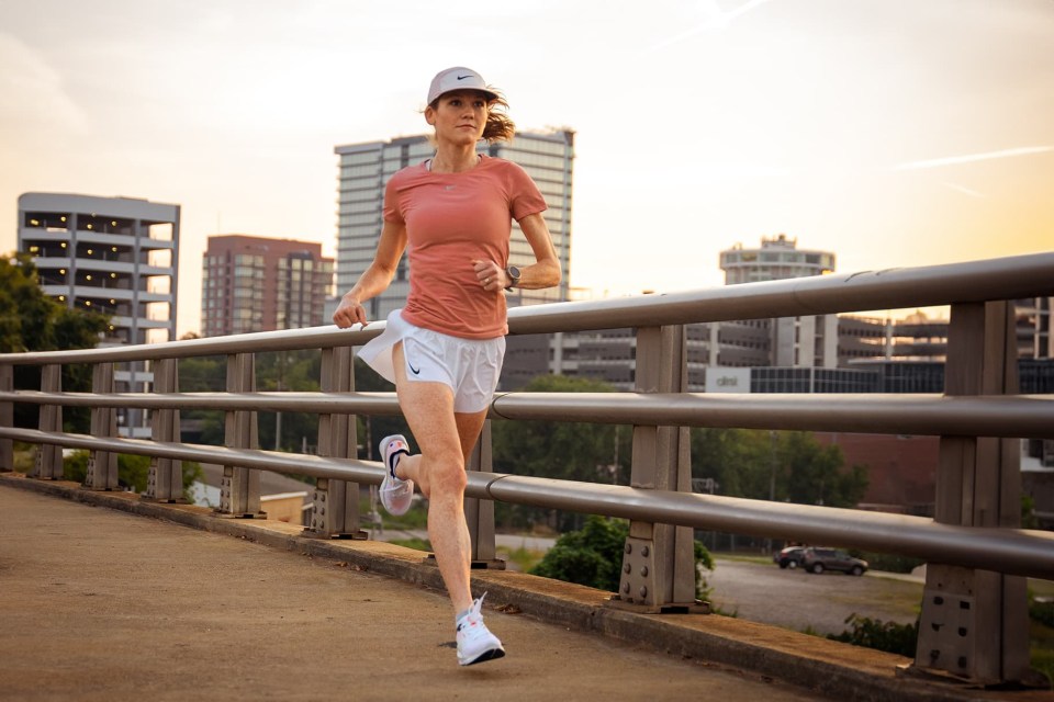 a woman wearing a nike hat is running on a bridge