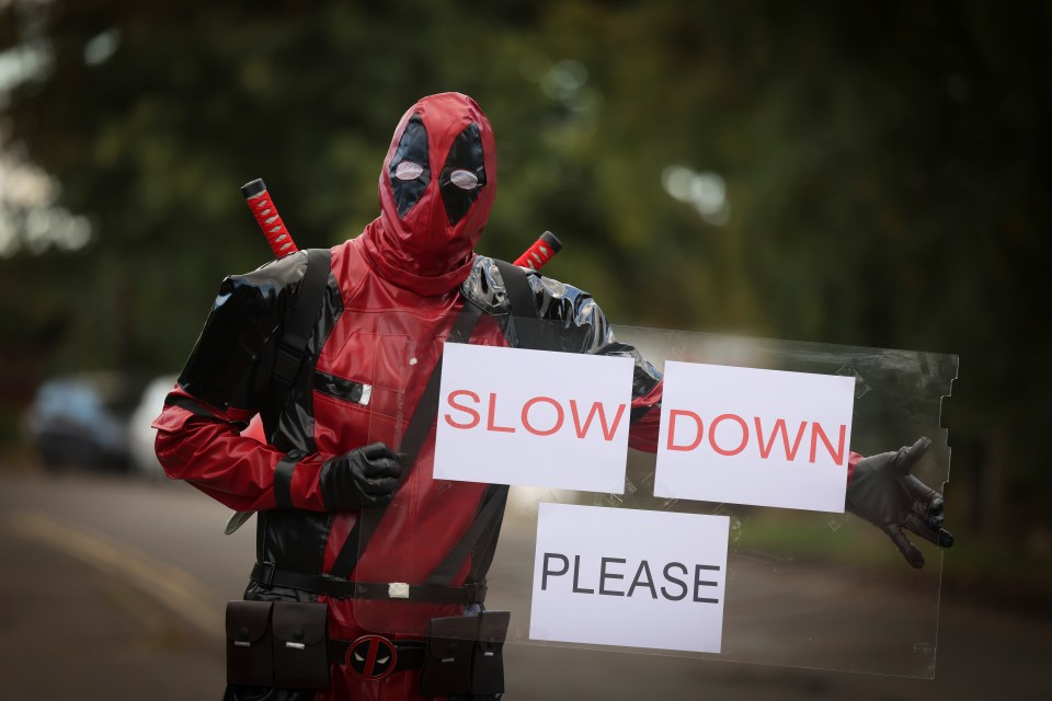 a man in a deadpool costume is holding a sign that says slow down