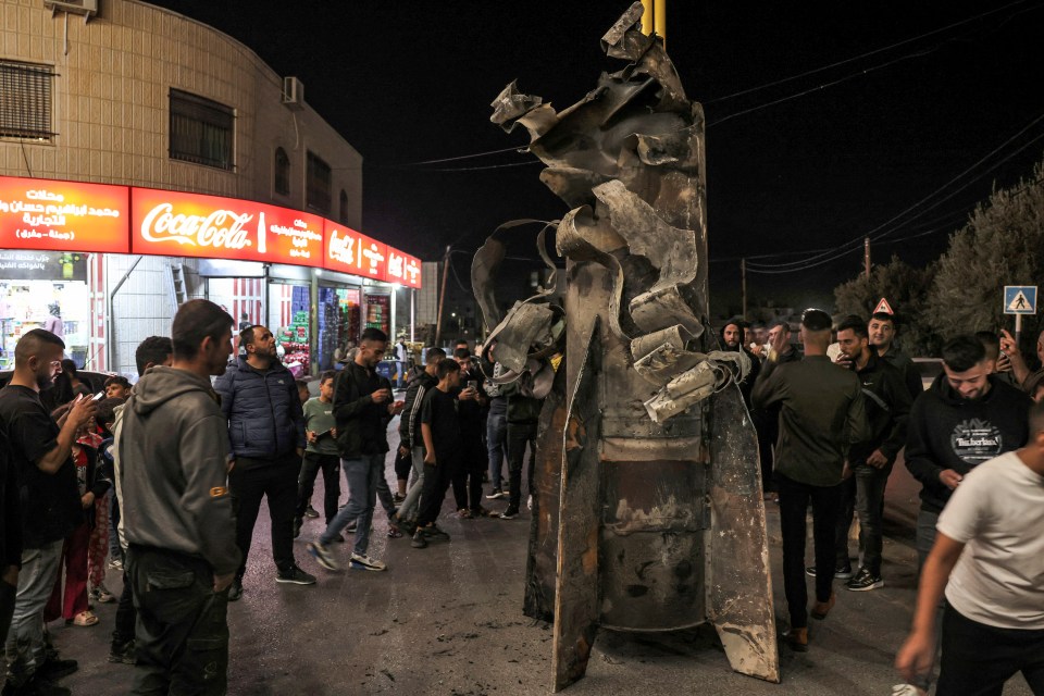 People gather around a fallen projectile that was moved to the centre of a square