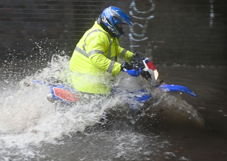 a man wearing a blue helmet and a yellow jacket is riding a dirt bike through a puddle of water