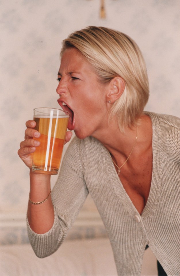 a woman is drinking a glass of beer with her mouth open