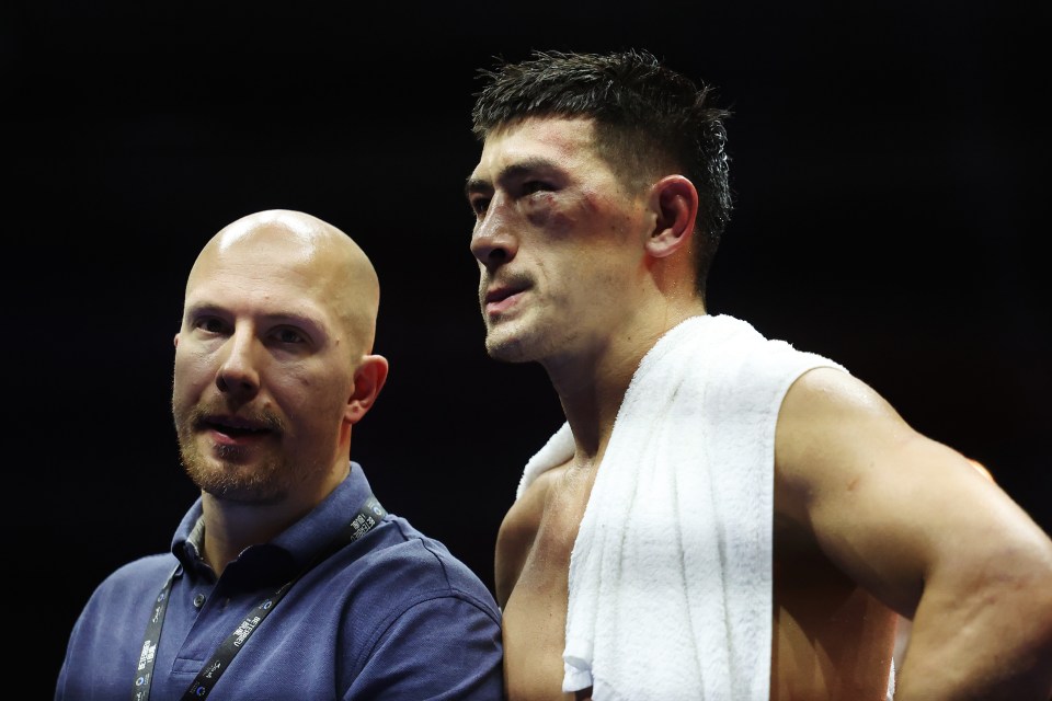 a bald man stands next to a man with a towel around his neck