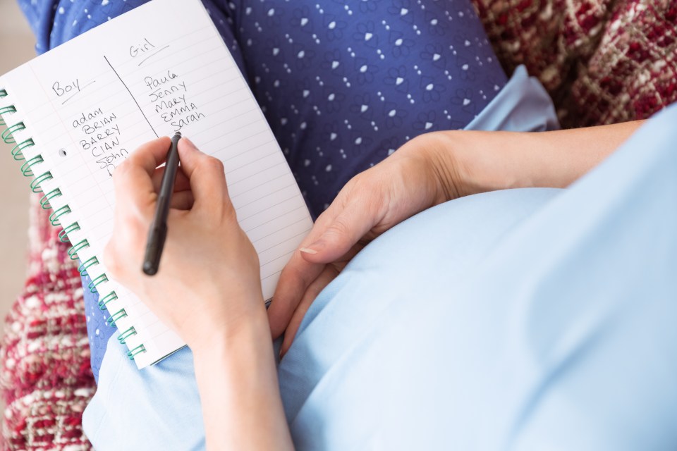 a pregnant woman is writing a list of baby names in a notebook