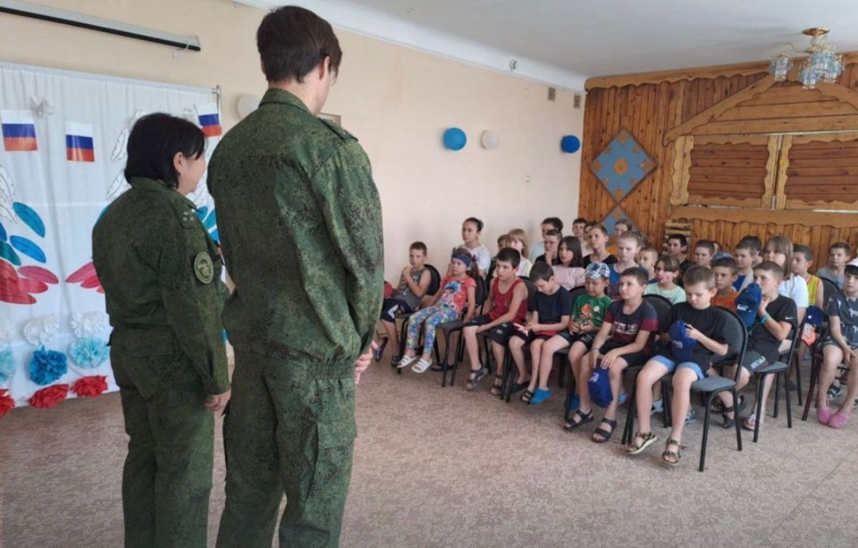 two people in military uniforms stand in front of a group of children