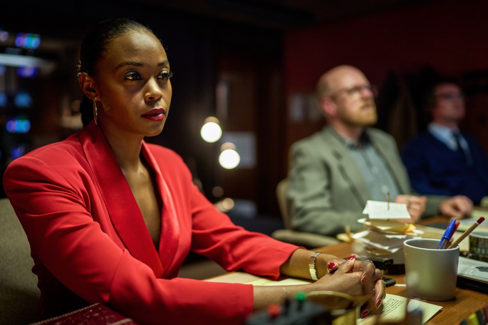 a woman in a red jacket sits at a desk