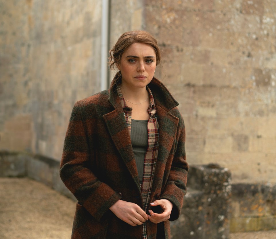 a woman in a plaid coat stands in front of a brick wall