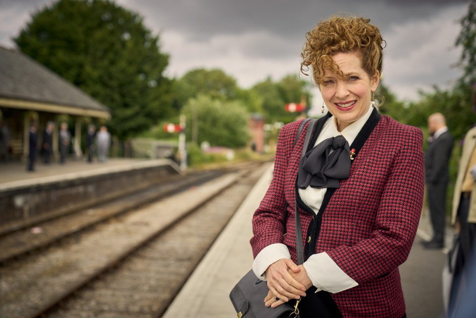 a woman in a red jacket is standing on a train platform