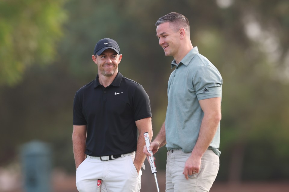 two men are standing on a golf course and one has a putter that says taylormade on it