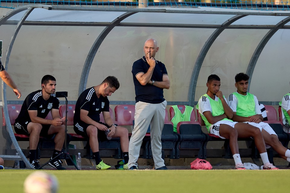 a group of soccer players are sitting in a dugout with a man covering his mouth