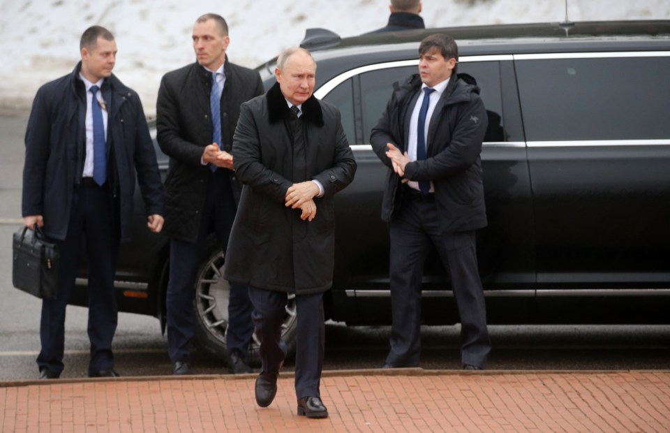 a man in a black coat is walking in front of a black limousine