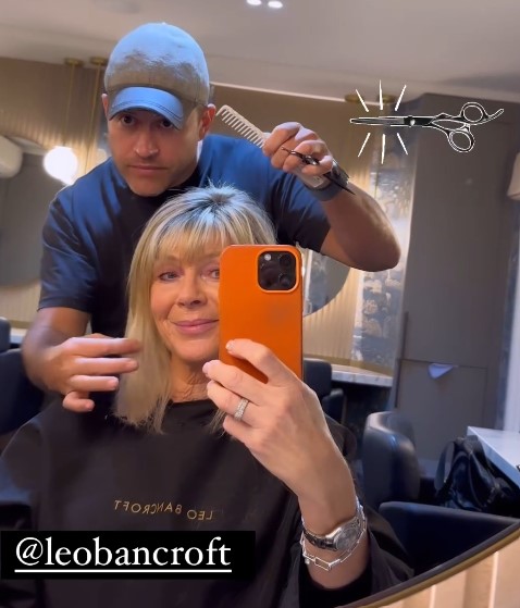 a woman is getting her hair cut by a man and taking a selfie