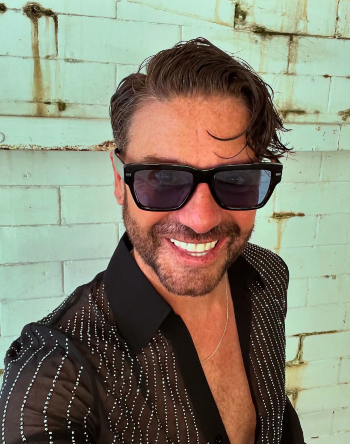 a man wearing sunglasses and a black shirt is smiling