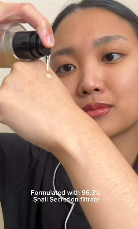 a woman is applying a product to her arm and the product is formulated with 96.3% snail secretion filtrate