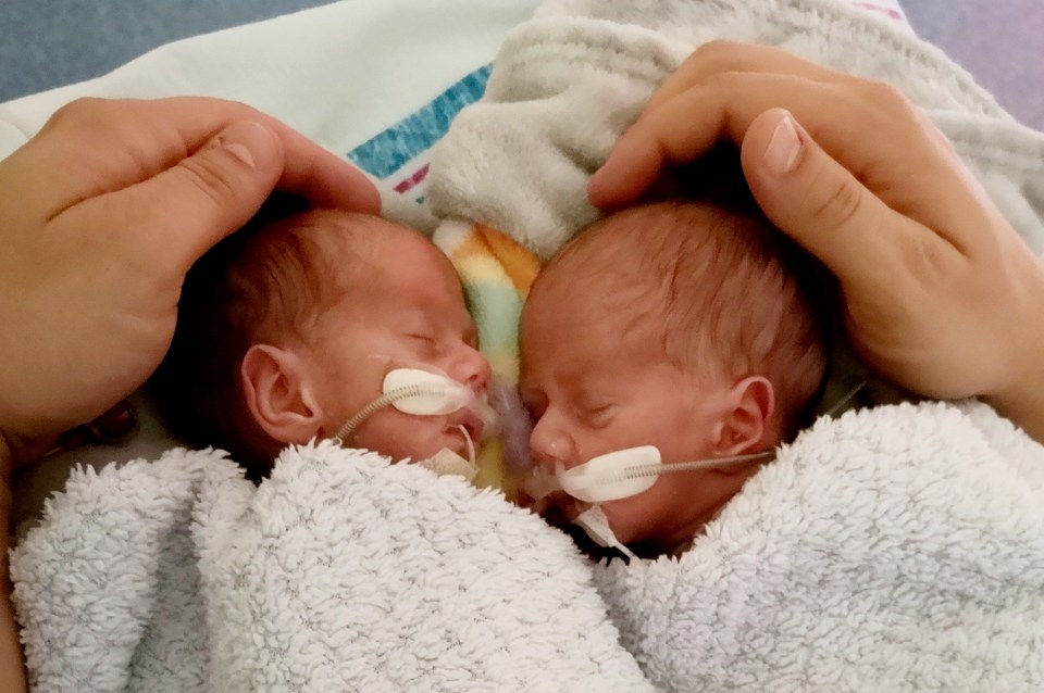 two newborn babies with tubes in their ears are being held by a person