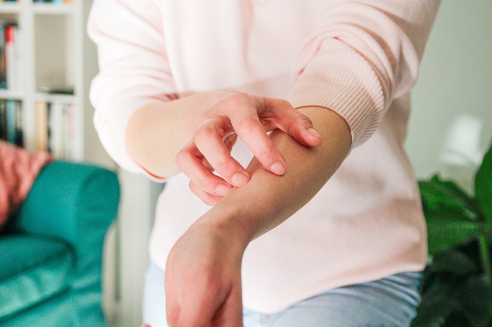 a woman in a pink sweater is scratching her arm