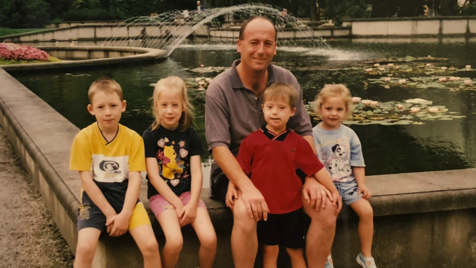 a man sits with three children in front of a fountain