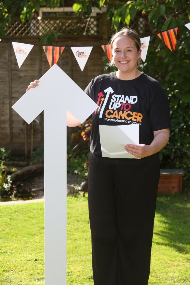 a woman wearing a black shirt that says " stand up to cancer "