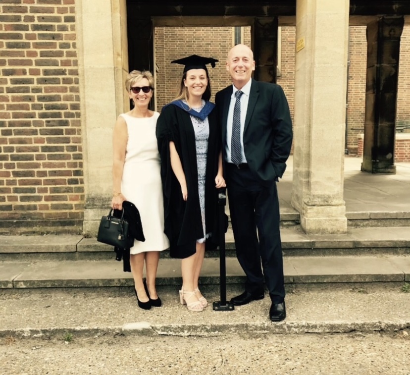 a woman in a graduation cap and gown poses with her parents