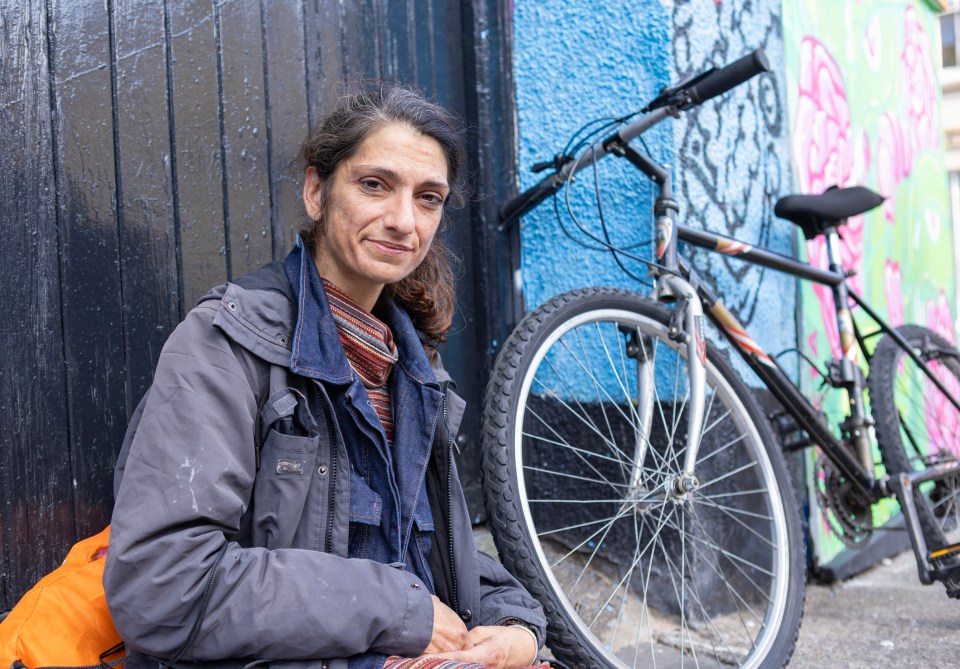 a woman leans against a wall next to a bicycle